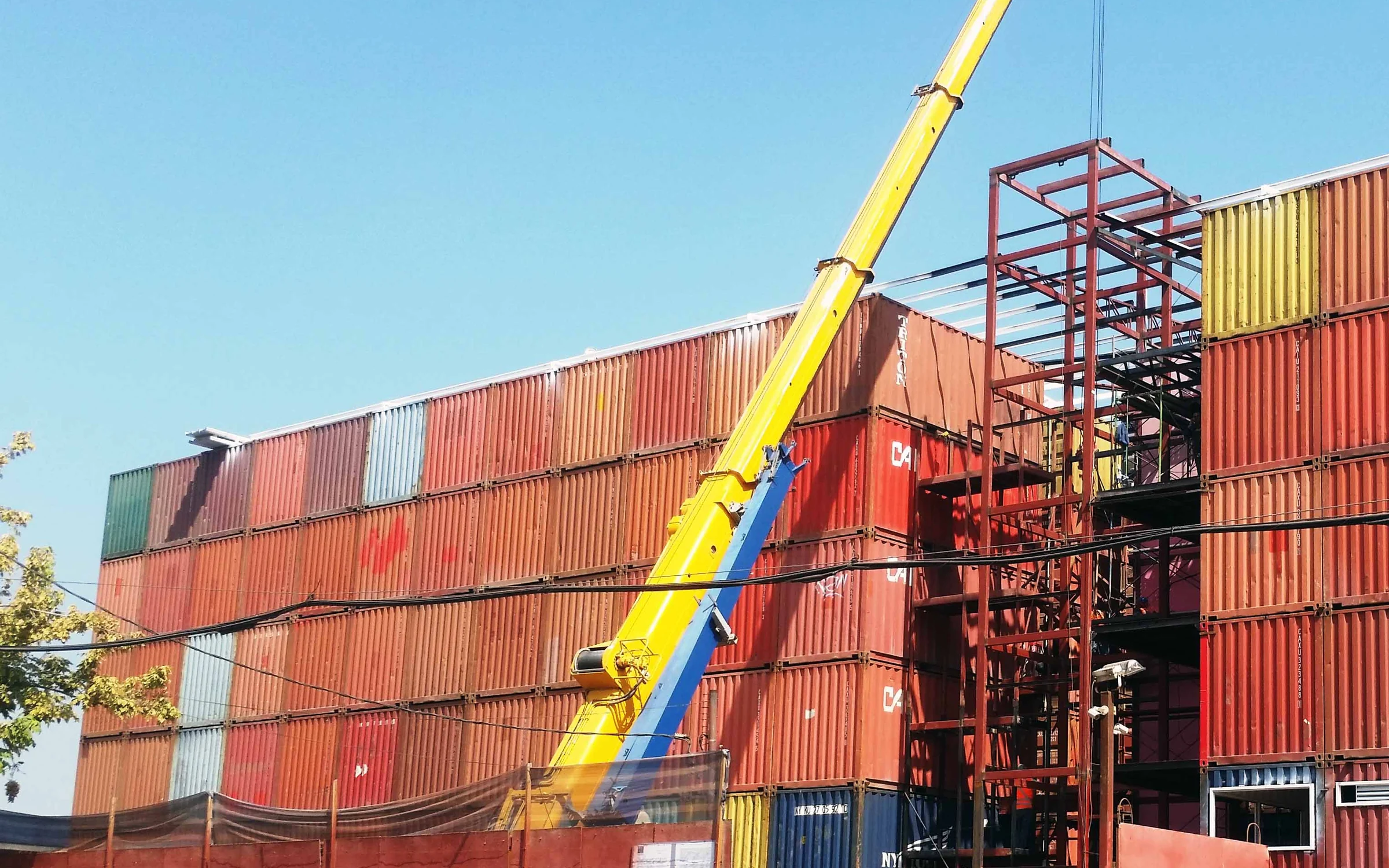 Montaje del Centro de Minibodegas BLT: fachada de contenedores marítimos apilados y grúa en obra